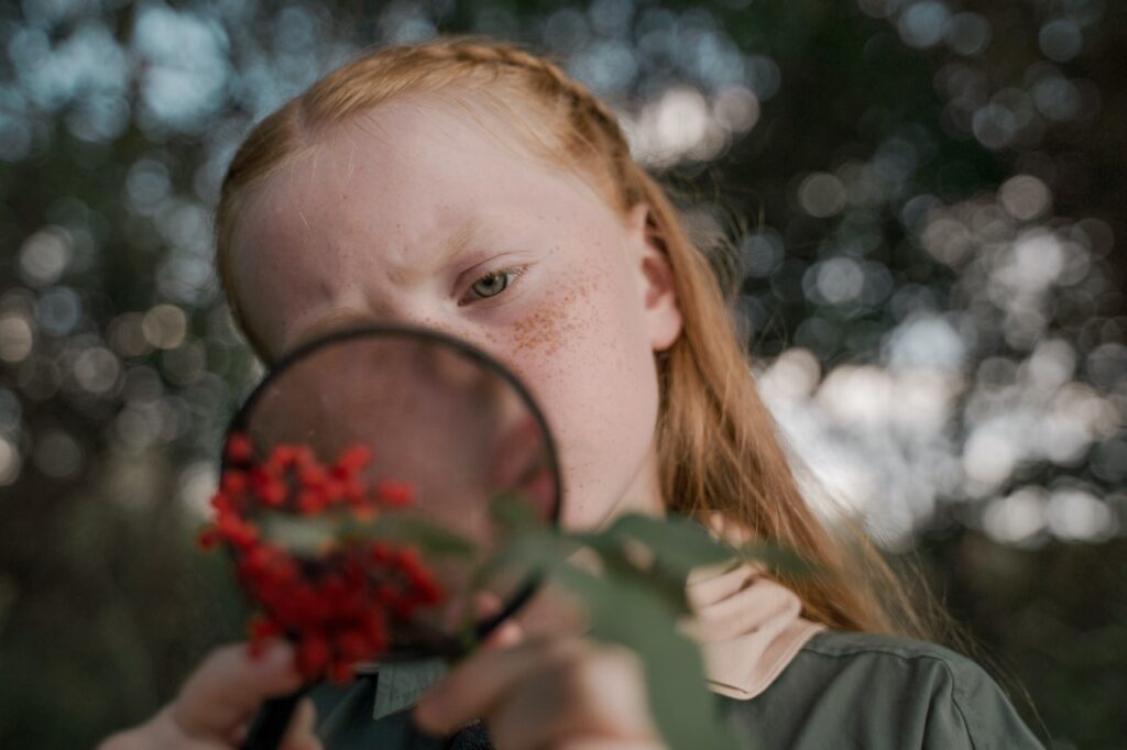 A girl looking through a magnifying glass at red berries in nature­