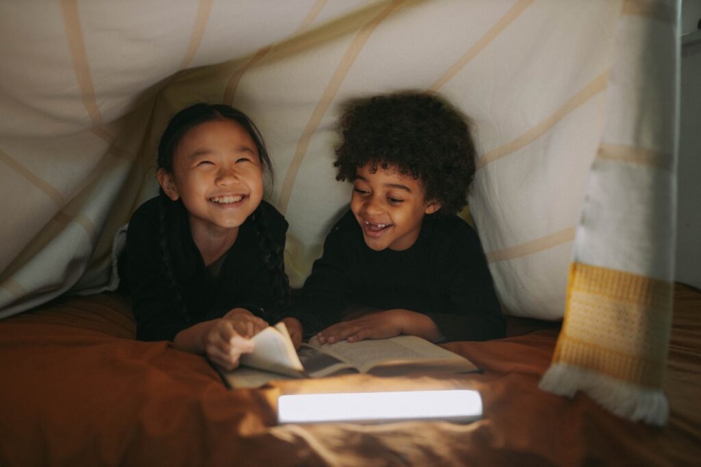 A boy and a girl laughing and reading in a tent