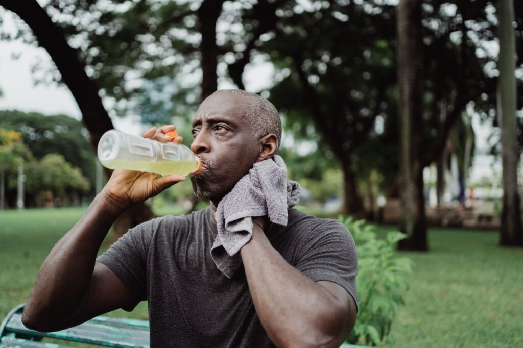 A man drinking flavored water while holding a cold rag next to his neck while trying to cool down