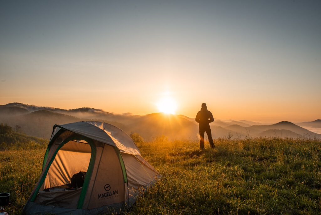 A person standing in a field near a tent watching the sunset