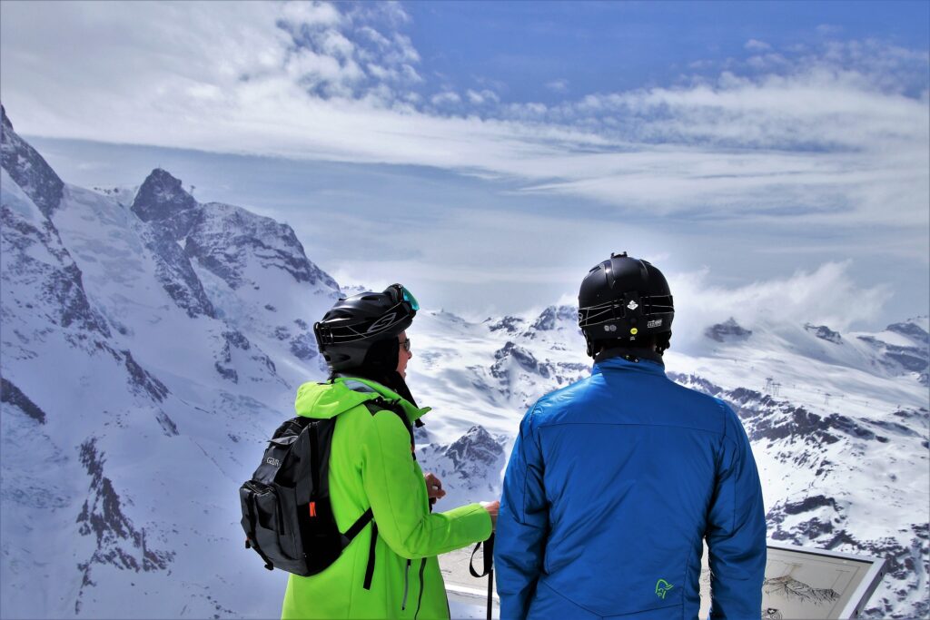  A couple of people in winter jackets looking at a mountain.
