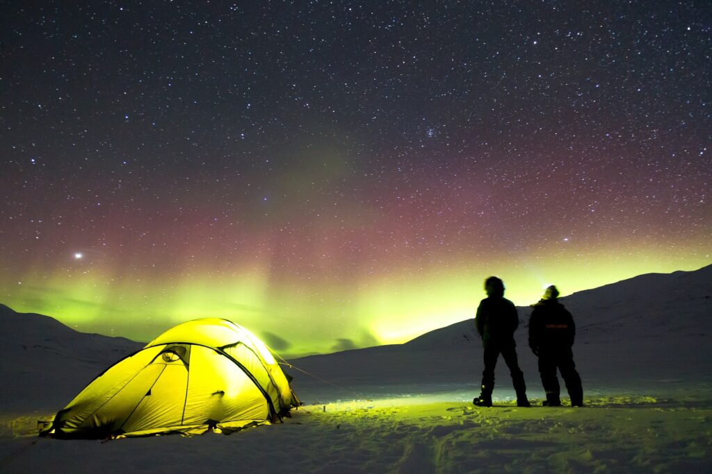 A couple of people standing next to a tent with a bright light in the sky above.